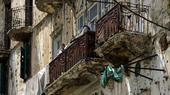 A boy looks out from the balcony of an apartment building marked with many bulletholes.