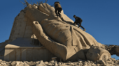 Zwei Männer klettern auf eine in Trümmern liegende Statue