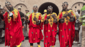 Vier Gnaoua-Musiker laufen durch Essaouira mit Kastagnetten und in roten Gewändern, die mit gelben und grünen Stickereien verziert sind.