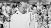 A man in a white robe holds up a communion wafer and breaks it.