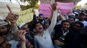 A group of men shouting with hands raised. Some hold signs with Urdu text.