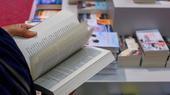 Hände, die ein Buch aufschlagen. Im Hintergrund verschwommen eine Bücherauslage.