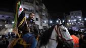 Ein Mann sitzt auf einem weißen Pferd und hält die neue syrische Flagge. Hinter ihm Gebäude in der Nacht.