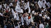 A crowd of people photographed from above, some holding flags with the words of the Shahada inscribed on them.