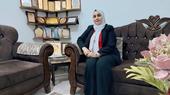 سيدة ترتدي الحجاب وتجلس على أريكة وخلفها رف من الدروع.
