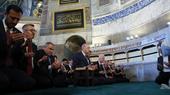 A row of men in suits pray in a mosque.