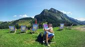 Ein Junge in Jeans sitzt in einem Sonnenstuhl vor einer Bergkulisse