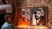 Two children stand beside a board holding portraits of Nelson Mandela and Yasser Arafat. Below the portraits are candles.