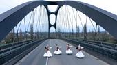 Auf einer bogenförmigen Autobahnbrücke tanzen vier Frauen in weißen Gewändern und langen dunklen Haaren.