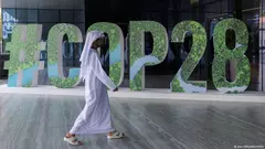 A person in Arab dress walks past a "#COP28" sign in Abu Dhabi, United Arab Emirates