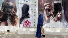 Eine verschleierte Frau läuft an einem Beauty-Salon vorbei. Die Gesichter der Frauen auf der Werbung an der Wand sind schwarz übermalt.