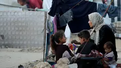 A mother sits with her children on the floor in a refugee camp in Gaza