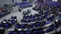 Annalena Baerbock stands at a podium in the centre giving a speech to a crowd of seated people wearing suits.