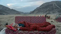 Eine alte Frau liegt auf einem Sofa, das in einer steinigen Landschaft steht.