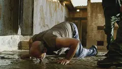 A man gets down on his knees, licking water.