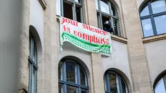 The facade of a building with a sign hanging from the windows reading "Your silence is complicity"