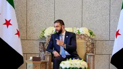 Der syrische Präsident al-Scharaa sitzt zwischen zwei syrischen Flaggen auf einem prachtvollen Stuhl.