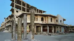 مبنى متهدم، أمامه ثلاثة أعمدة تاريخية مزخرفة.