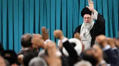 Ali Khamenei steht vor einer Menge Zuhörer und hebt die linke Hand