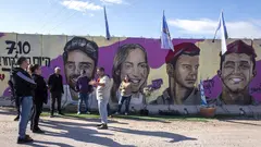 Eine Gruppe steht vor einer Betonmauer. Auf der Mauer sind farbige Portraits von israelischen Geiseln zu sehen.