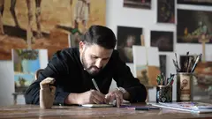 A man sits at a desk writing in a notepad.