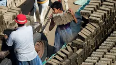 طفل وبجواره رجل يضعان قطع الطوب على عربة يجرها حمار.