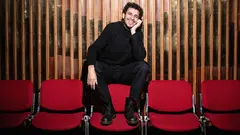 a man wears a black outfit and sitting on chair.