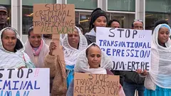 Women in traditional Eritrean clothing hold up signs reading: "Stop Criminal Human Trafficking Network"