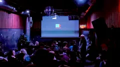 A crowded room full of people. On a screen at the front, the words "Palinale" and a logo.