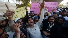 A group of men shouting with hands raised. Some hold signs with Urdu text.