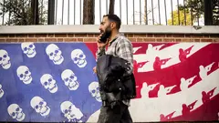 Ein Mann läuft vor einer Mauer mit einem Anti-Amerika-Graffiti