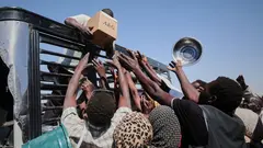 A group of people reach for a box of aid being handed down from a truck.