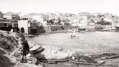 Black and white image of the Beirut seafront, with a sailing boat in the centre.