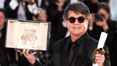 A man wearing a black suit and sunglasses holds an award and a scroll.