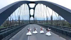 Auf einer bogenförmigen Autobahnbrücke tanzen vier Frauen in weißen Gewändern und langen dunklen Haaren.