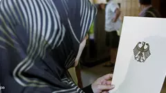 Woman wearing the headscarf looking at a sheet showing the heraldic eagle of the Federal Republic of Germany (photo: picture alliance/dpa)