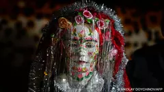 The bride's hair is covered with a red headscarf, her painted doll-like face framed with silk flower garlands and streaks of shiny tinsel, making her unrecognisable. She is then presented to her husband-to-be clad in traditional attire of dark crimson baggy pants, multi-coloured apron and bodice and henna-painted fingertips contrasting with his simple blue jeans and black blazer. 