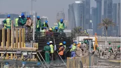 عمال وافدون أثناء عملهم في إنشاء أحد إستادات كأس العالم وفي الصورة تظهر ناطحات السحاب في الدوحة. (أرشيف 21 /12 /2014).