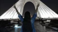 فتاة كاشفة الرأس تقف أمام برج آزادي في طهران تظهر علامة النصر بكلتا يديها  نوفمبر  / تشرين الثاني 2022 - إيران.