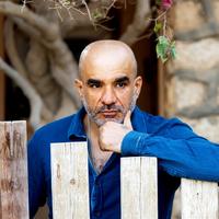 Youssef Rakha. (Photo: private) A man with his hand on his chin stands leaning against a wooden fence.