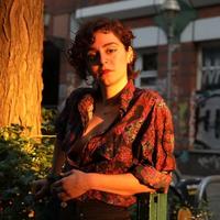 Eine Frau im Abendlicht lehnt an einem Zaun, hinter ihr Graffiti.