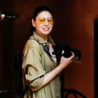 Eine Frau mit orangener Sonnenbrille und Kamera in der Hand schaut seitlich in die Kamra.
