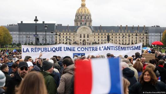 Thousands of people stand in a public square. Someone holds up a French flag and in the background, people hold a banner saying: "The Republic united against anti-Semitism"