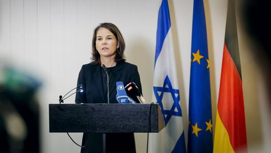 Baerbock makes a statement in front of an Israeli flag, a European flag and a German flag.