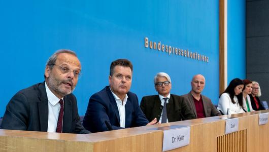 Sieben Männer und Frauen sitzen als Sprecher:innen im Raum der Bundespressekonferenz