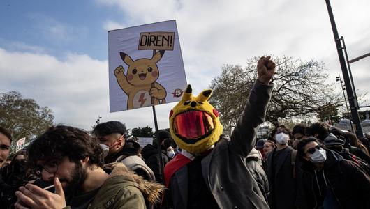 A crowd of people at a demo. One man is wearing a pikachu helmet with reflective visor.