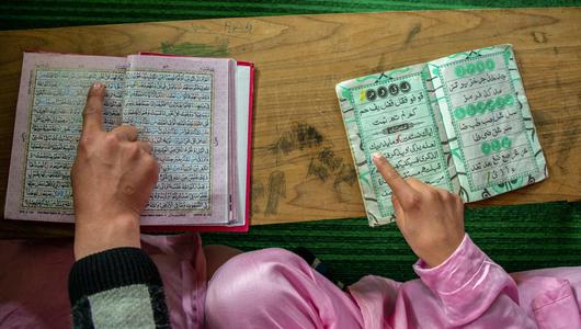 Two people point their fingers at two copies of the Qur'an. Photo from above, only the hands visible.