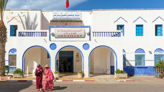 Two women wearing traditional clothes leave a hospital building designed in Art Deco colonial style.
