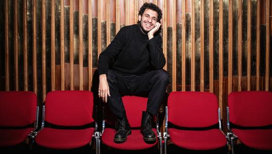 a man wears a black outfit and sitting on chair.