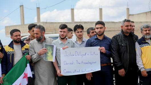Eine Gruppe Männer hält Plakate und die neue syrische Flagge. Plakat: "Justice Delayed is Justice Denied! The Assad regime's crimes will not be forgotten."
